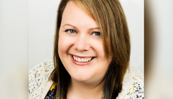 Patient Advocate Lori, a smiling woman in a crocheted sweater with shoulder-length brown hair, whose spouse has PI